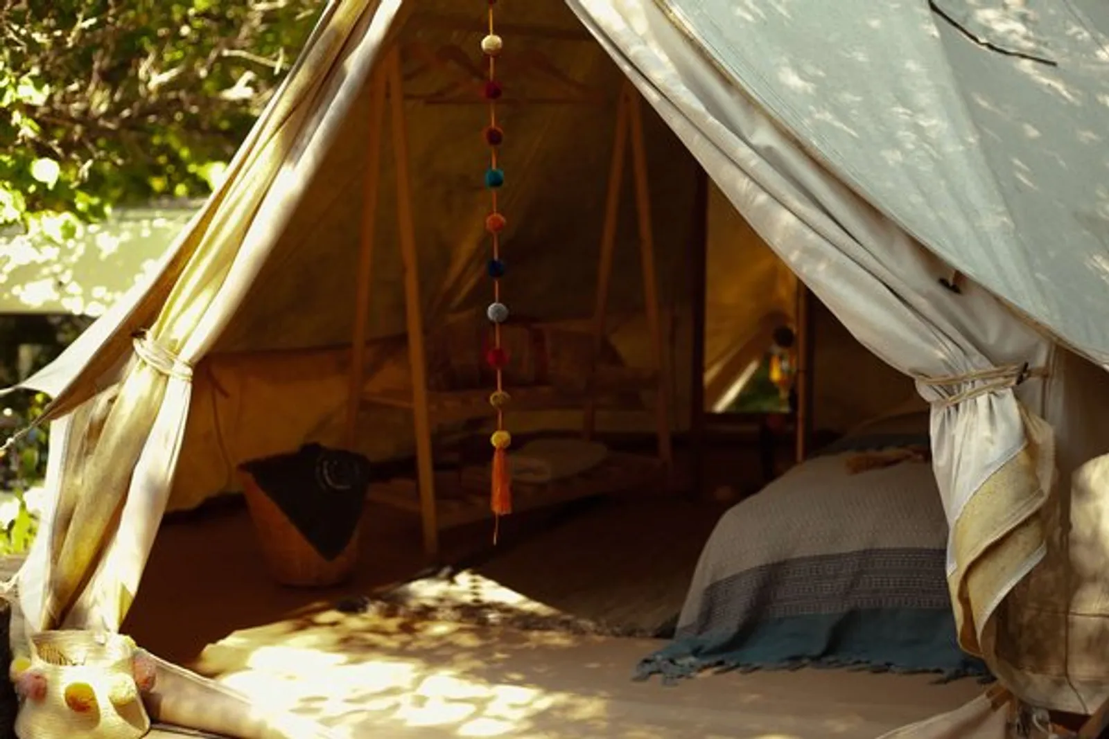 Hi-Five Tent: canvas tent under the trees with a garland at the entrance