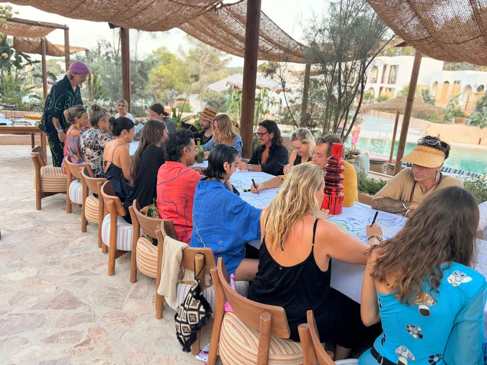Guests seated opposite one another drawing on a shared paper-covered table beneath a woven canopy.