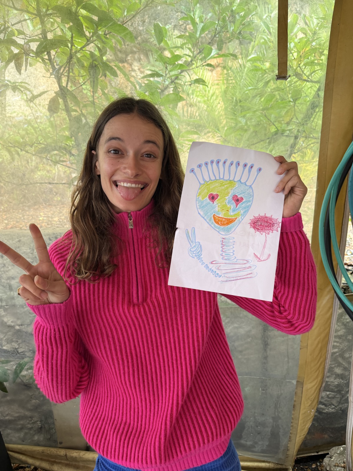 Participant in a pink sweater holding a colourful antennaed alien drawing