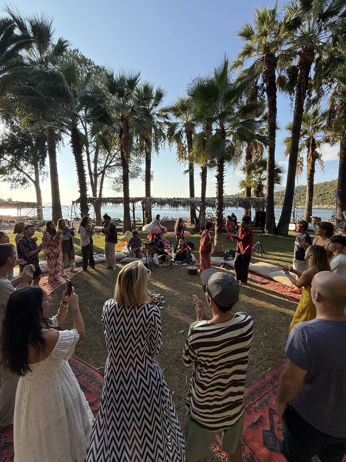 People gathered in a circle under palms beside the sea