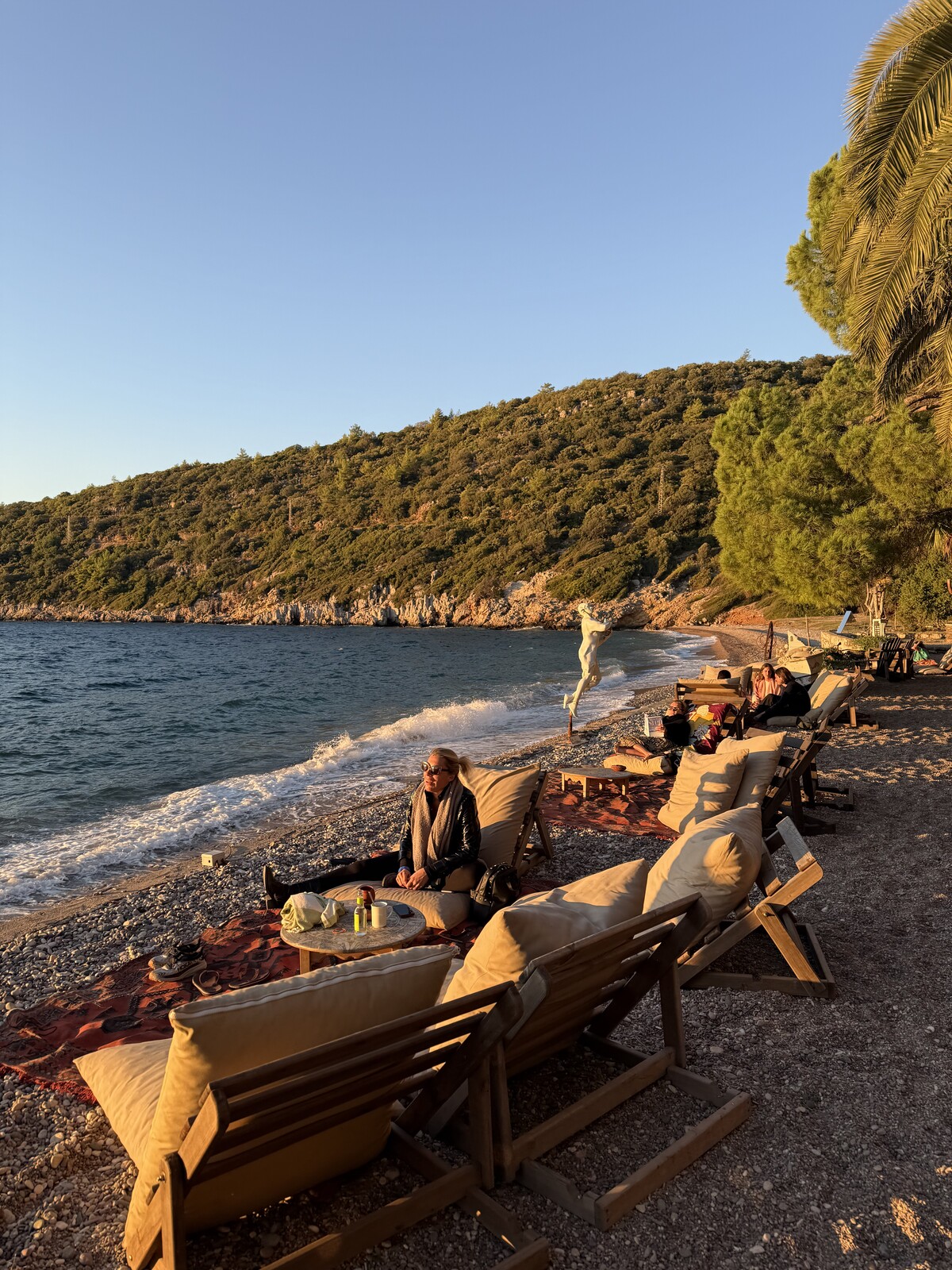 Sunlit beach seating beside the water and green hillside at Bonjuk Bay